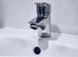 Homeowner examining a bathroom sink faucet for a leak with tools on the counter nearby.