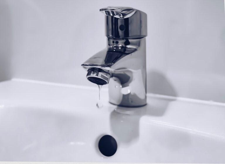Homeowner examining a bathroom sink faucet for a leak with tools on the counter nearby.