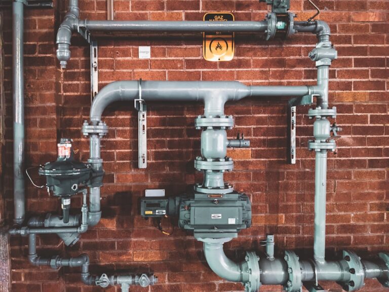 A commercial maintenance technician checks for leaks on exposed water pipes in a building utility room.