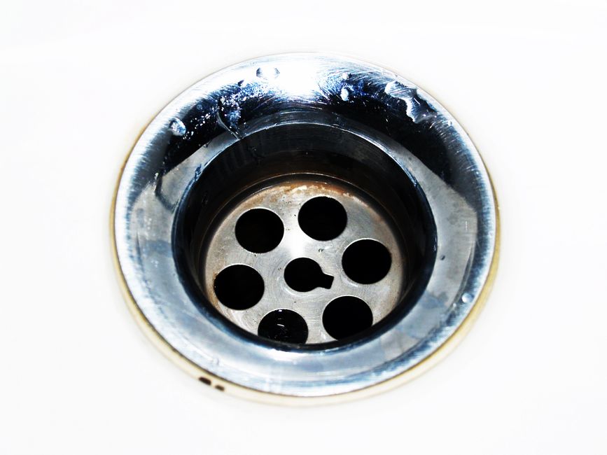 A person wearing gloves uses a hand auger to clear a bathroom sink drain.