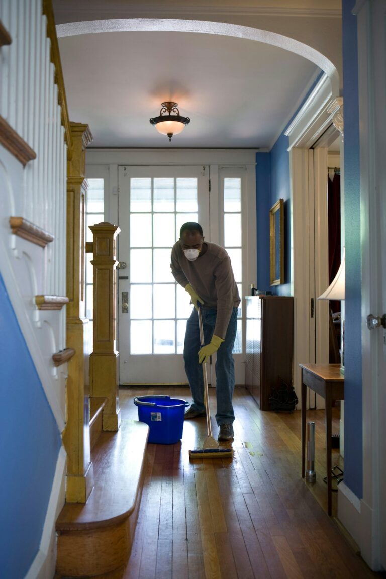A person checking a clipboard and inspecting a home's exterior siding and gutters.