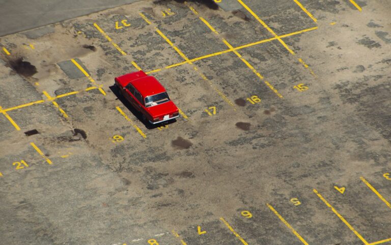 Maintenance workers inspect a commercial parking lot with potholes, standing water, cracked asphalt, and drainage grates.