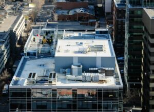 Technician inspecting rooftop HVAC equipment beside a commercial office building with tools and access panels open