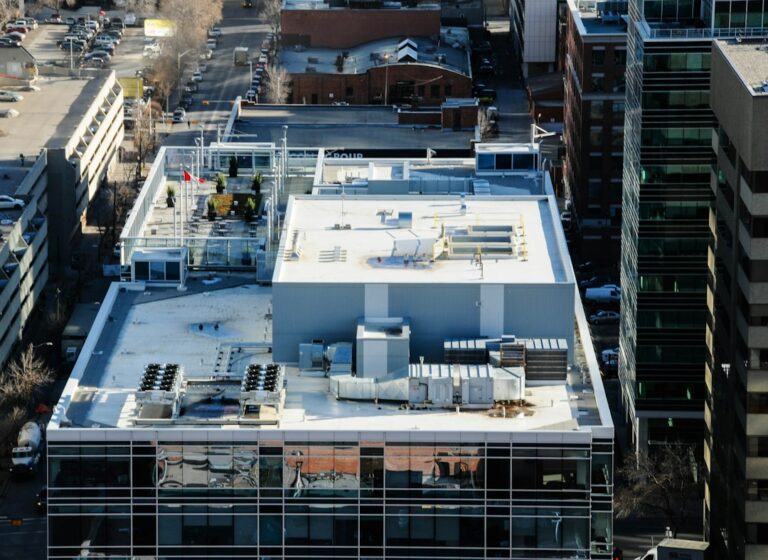 Technician inspecting rooftop HVAC equipment beside a commercial office building with tools and access panels open